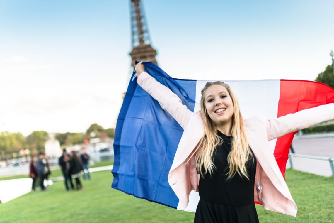 Chica con bandera de Francia delante de Torre Eiffel