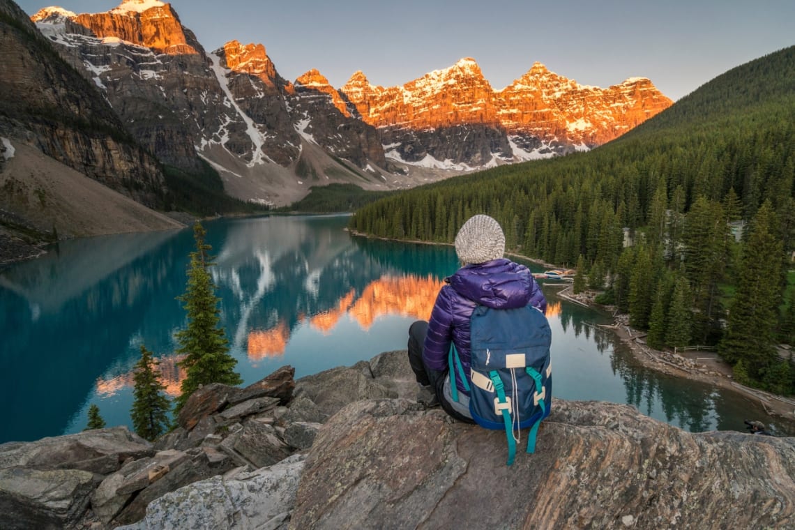 Chica con mochila mirando hacia lago y montaña en Canadá