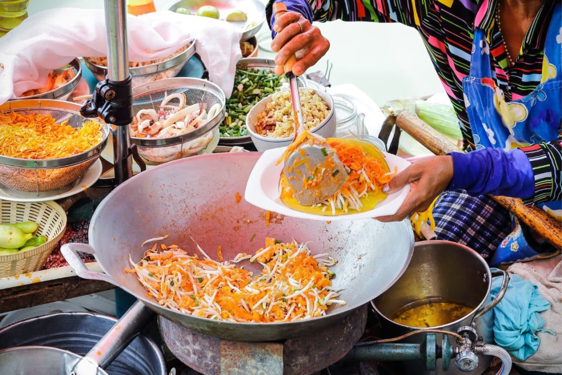 Mujer sirviendo pad thai desde un wok en puesto de comida callejera