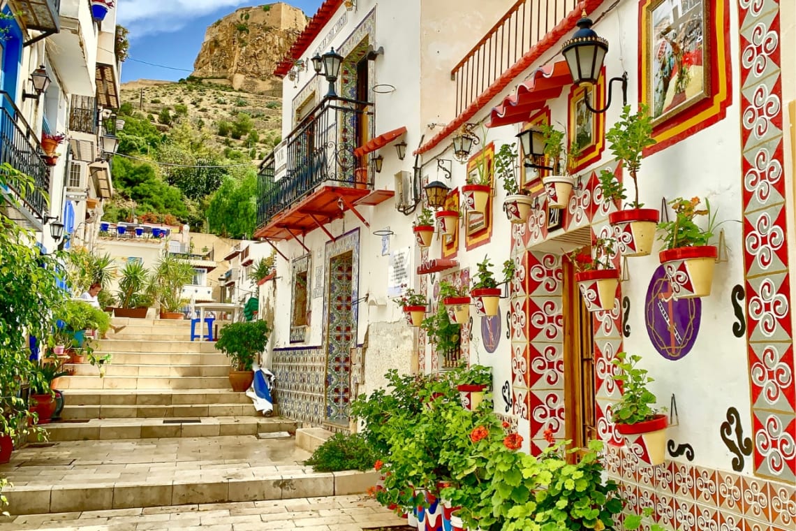 Pasaje con casas coloridas con muchas plantas y vista del castillo al fondo