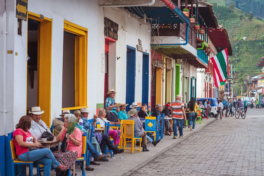 Calle empedrada con gente sentada en la vereda frente a construcciones coloridas en Jardín