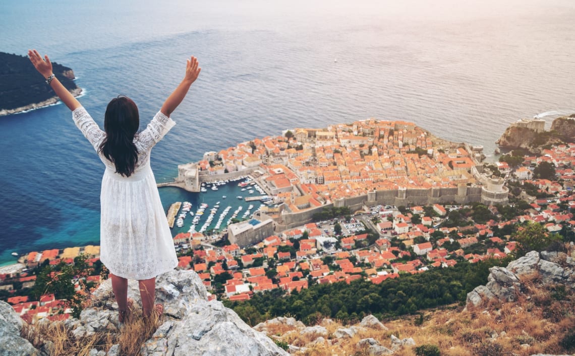 Girl looking at Dubrovnik old city from a viewpoint with arms up 