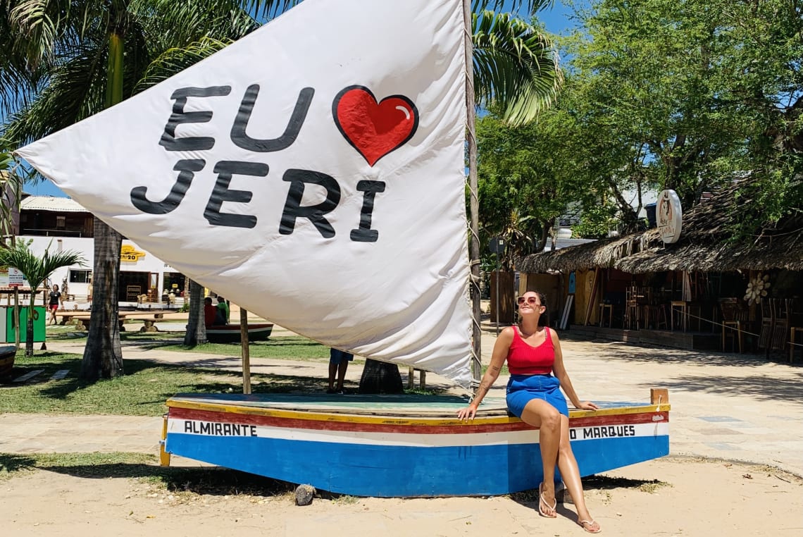 Mulher posando em pequena jangada que diz "Eu amo Jeri" na vela