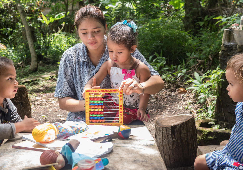 Cuidado de niños: joven haciendo juegos de aprendizaje con tres niños pequeños