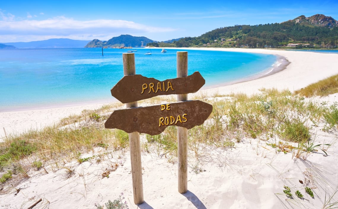 Cartel de "Playa de Rodas" y playa con agua turquesa detrás