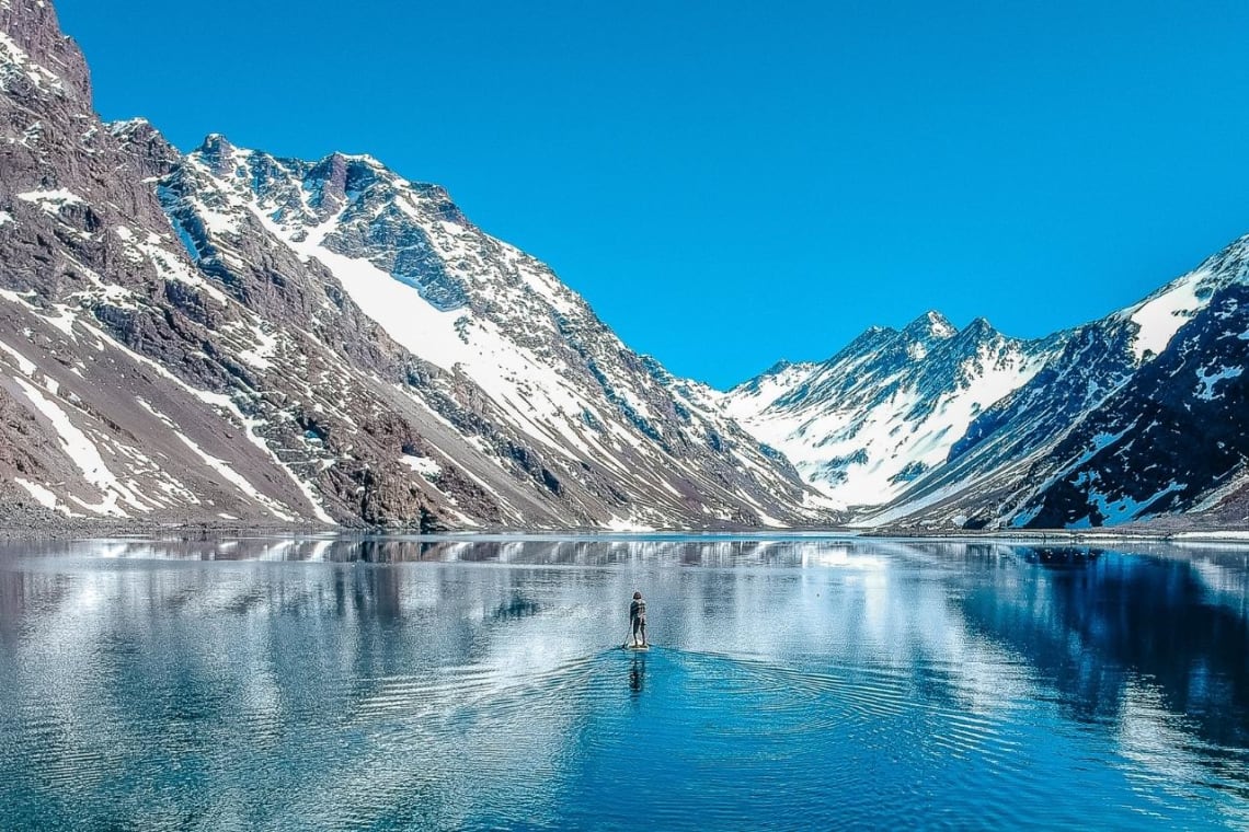 Chica haciendo stand up paddle en una laguna entre montañas nevadas