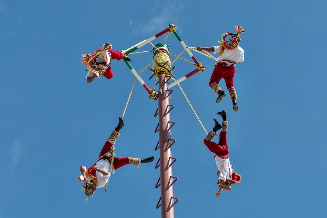 Four men hanging upside down from a pole for the Danza de los Voladores ("Dance of the Flyers") in Mexico