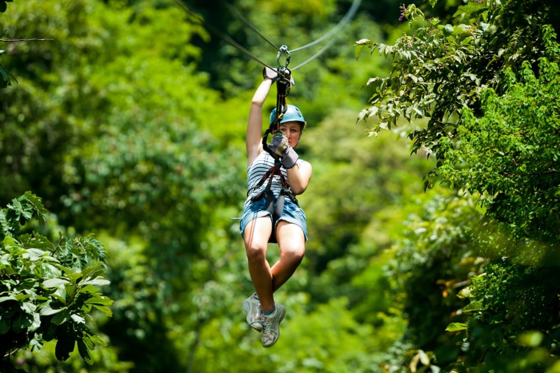 Cuánto cuesta viajar a Costa Rica: chica tirándose en tirolesa por la selva.