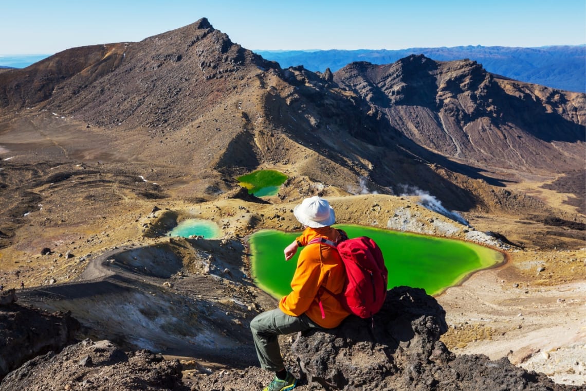 Senderista descansando frente a lagos volcánicos en trekking de Tongariro