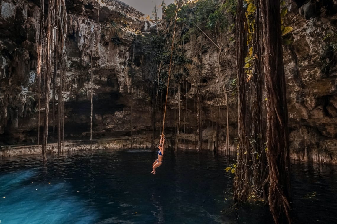 Chica tirándose al cenote colgando de una soga