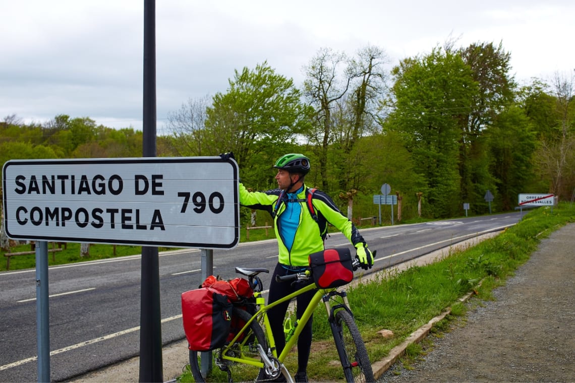 Ciclista en Francia junto a cartel que indica que faltan 790 km para Santiago de Compostela