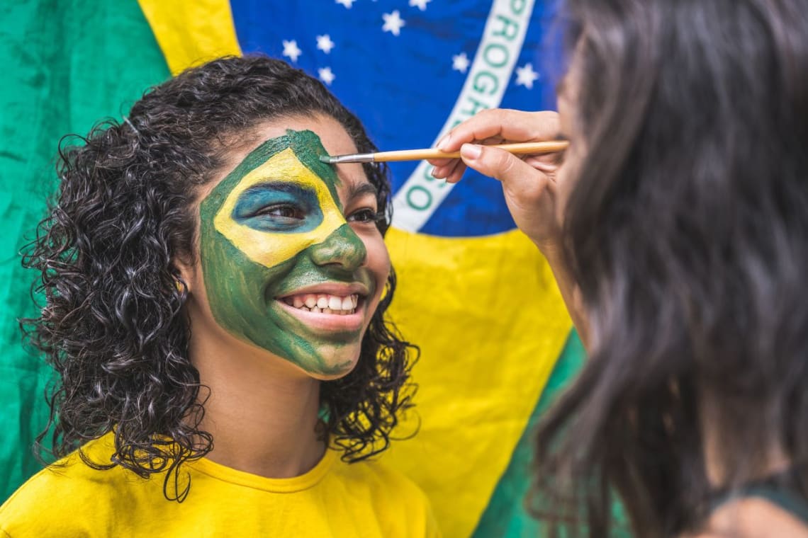 Chica siendo pintada en la cara con bandera de Brasil