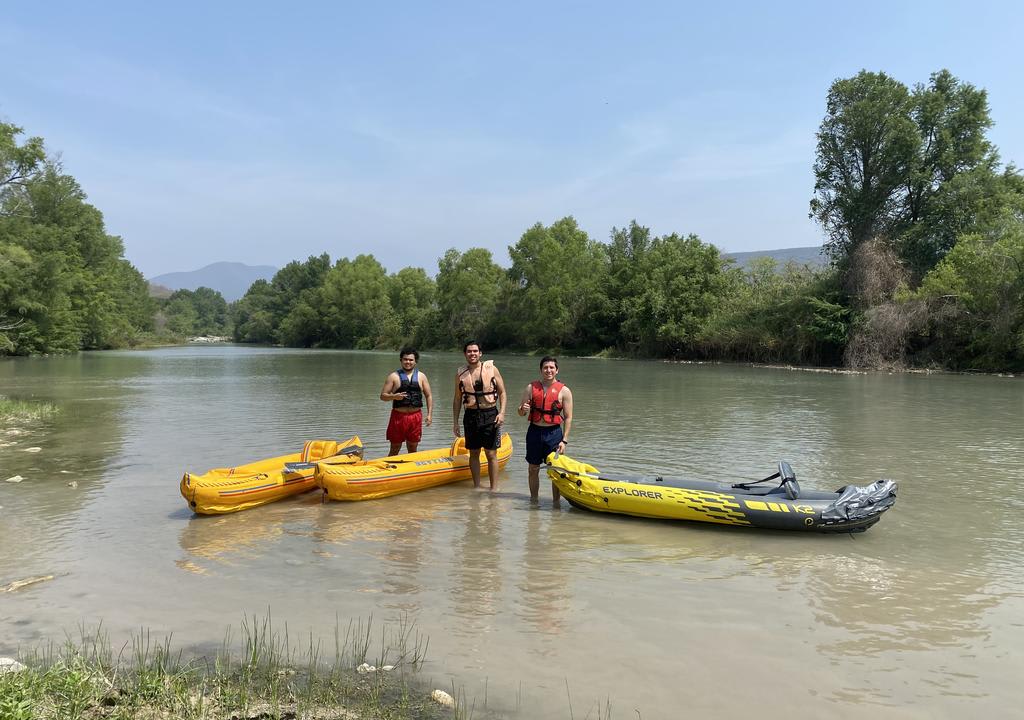 Three guys standing next to their kayaks in a river