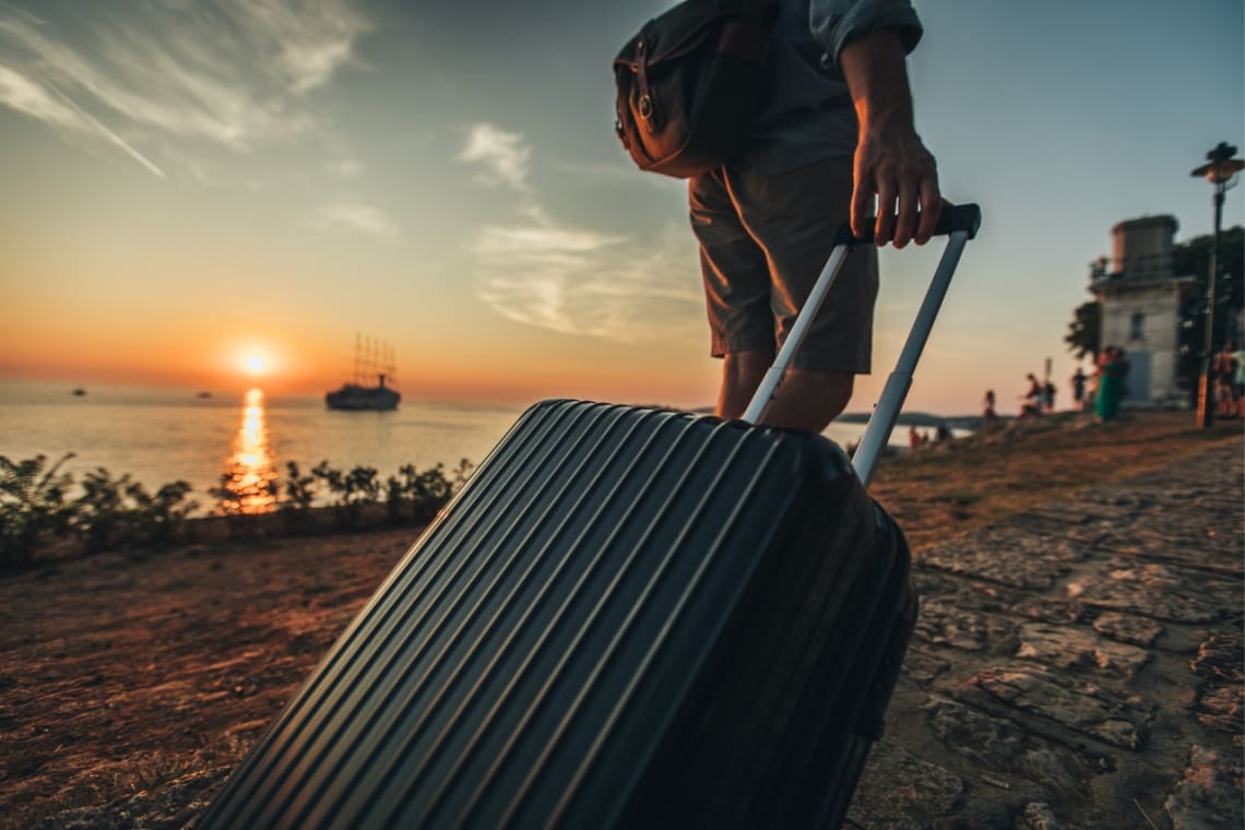 Hombre caminando con su maleta por una calle al costado del mar 