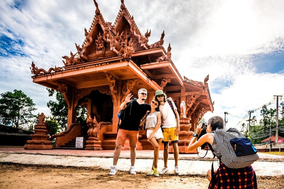 Group of friends posing for a photo in front of a temple in Thailand, a great destination for a vacation alone