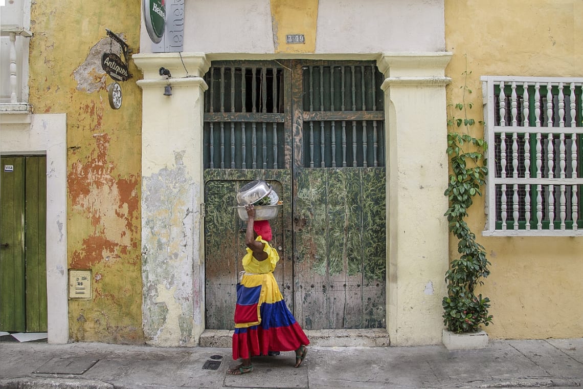 Mujer en vestido tradicional caminando frente a casa colonial
