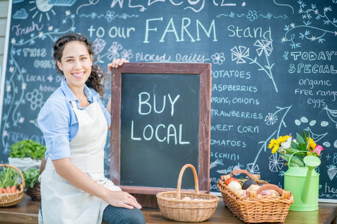 Girl at a farm stand holding a sign that says "Buy local"