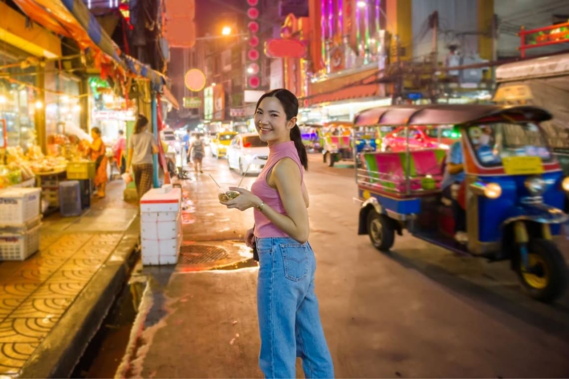 Girl with finger food walking the streets of Bangkok at night