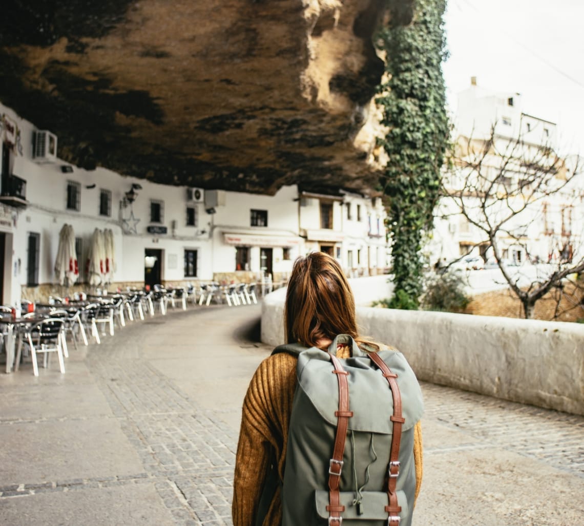 Girl with a backpack walking in a walkway under a rock in Setenil de la Bodega, Spain