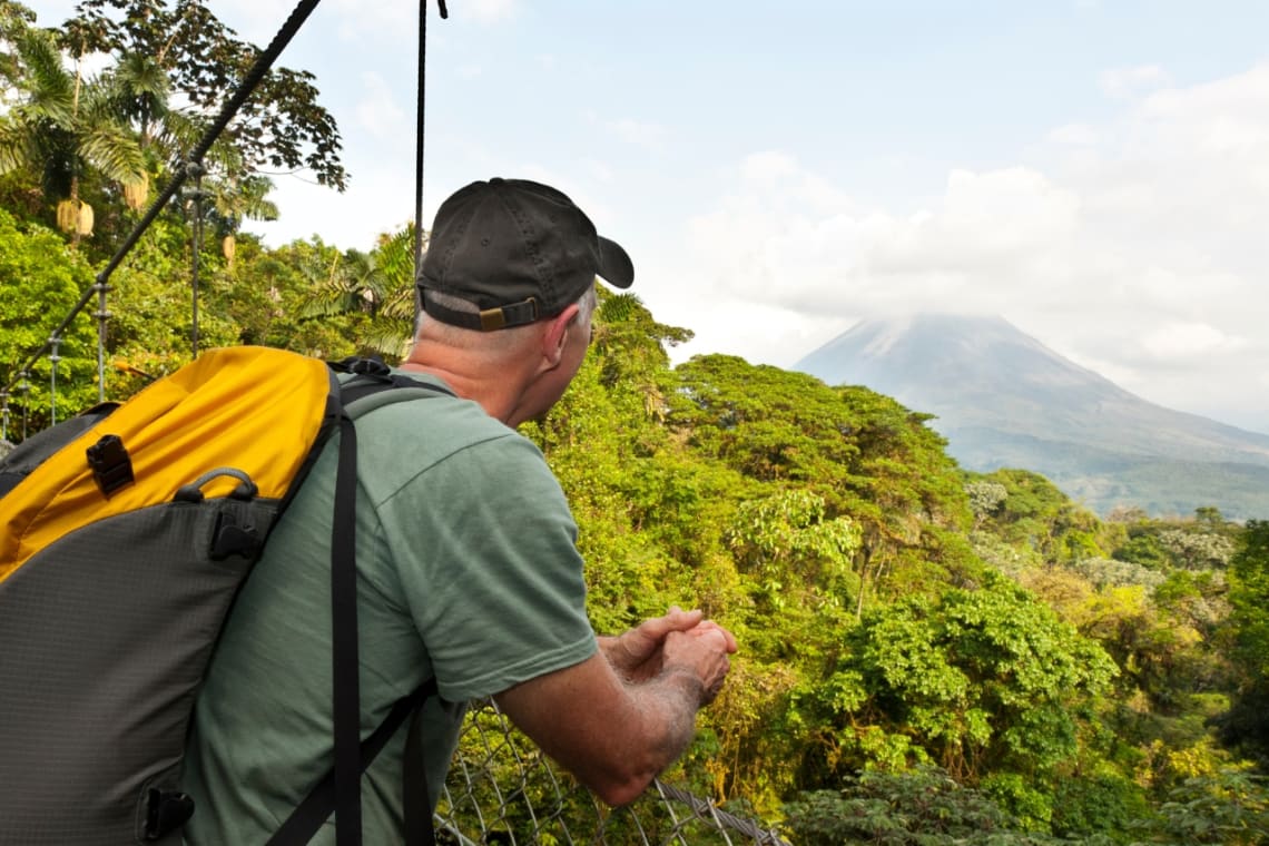 Hombre mirando a la selva y al volcán Arenal desde un puente elevado