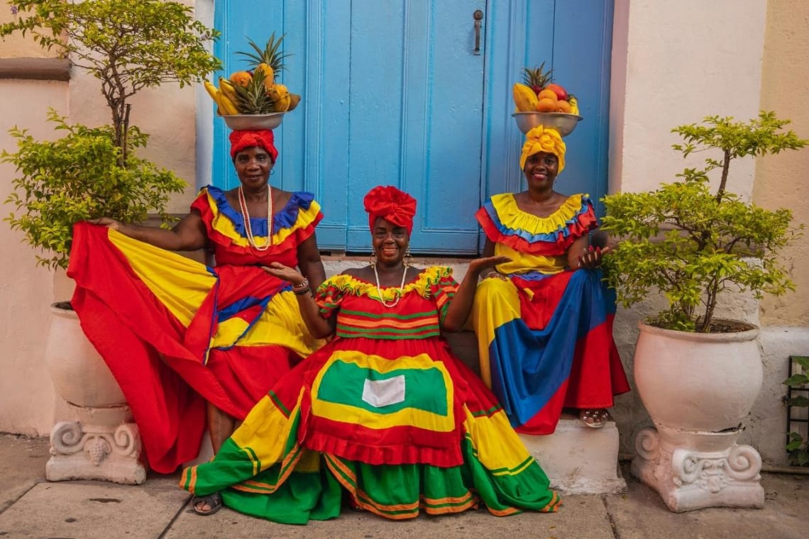 Tres mujeres colombianas con colorida vestimenta tradicional y canastas con frutas en la cabeza