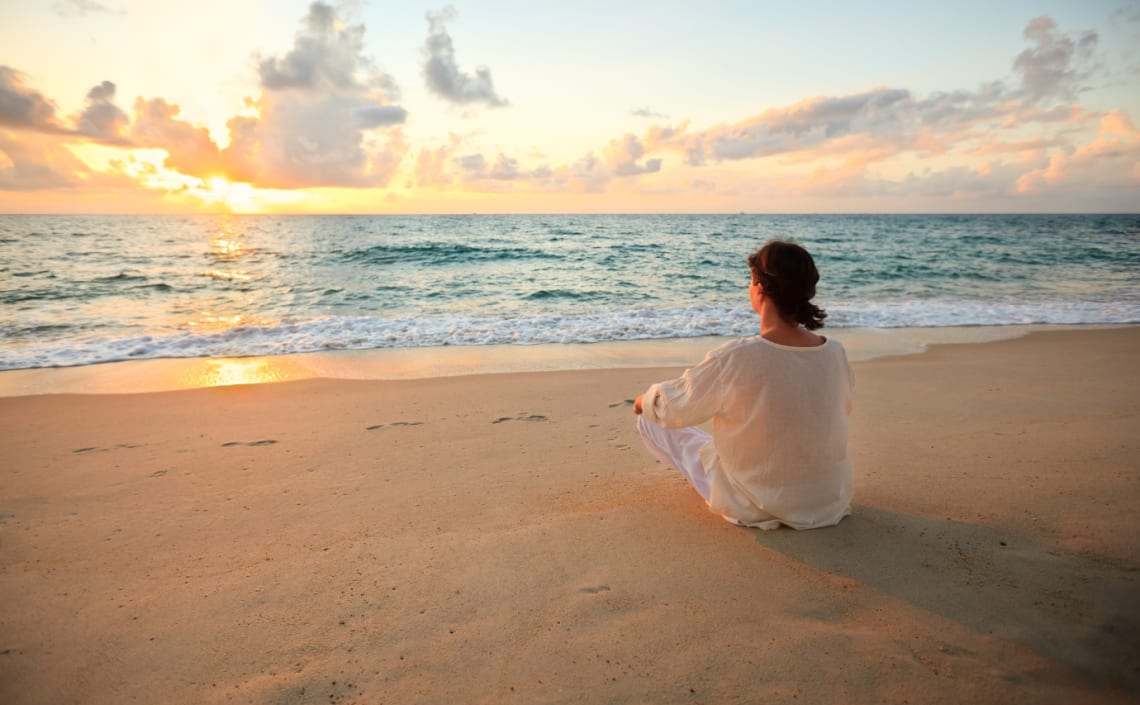 Chica sentada en una playa tranquila viendo el atardecer