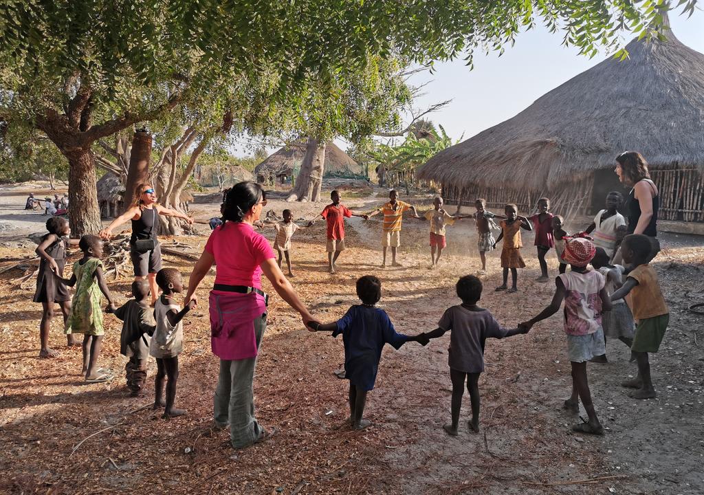 Three western women playing with kids of a rural village of Africa