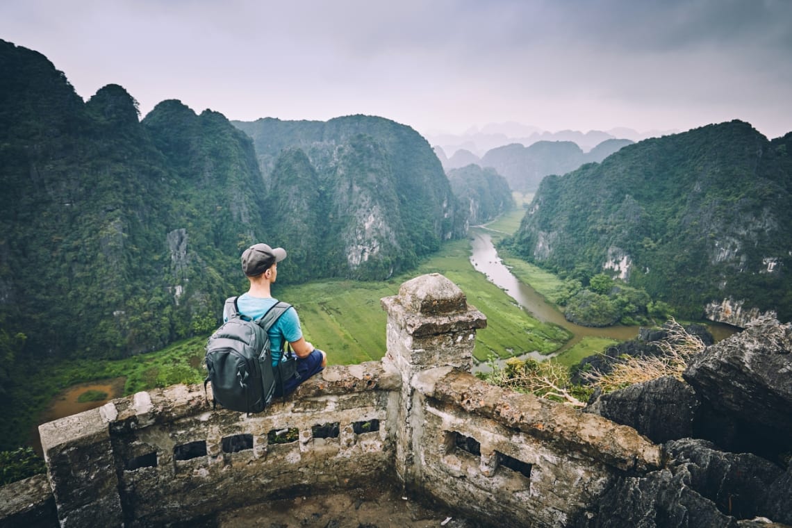 Joven sentado mirando desde lo alto hacia paisaje de montañas kársticas en Vietnam, Sudeste Asiático