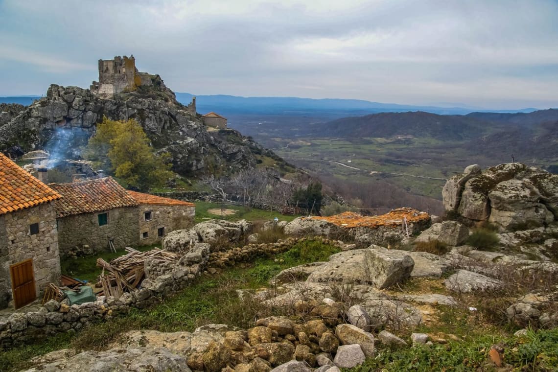 Paisaje montañoso con casas de piedra y castillo a lo lejos en Extremadura