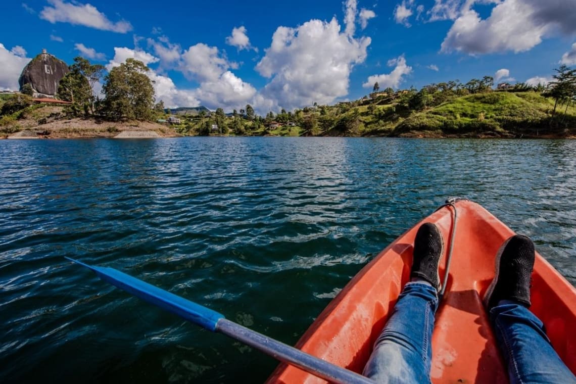 Hombre haciendo kayak en lago con vista al Peñón de Guatapé