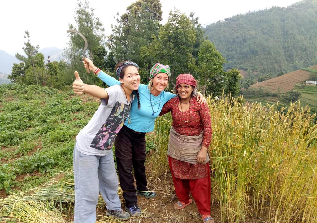 Dos voluntarias abrazadas con una mujer nepalí en zona de montañas con plantaciones