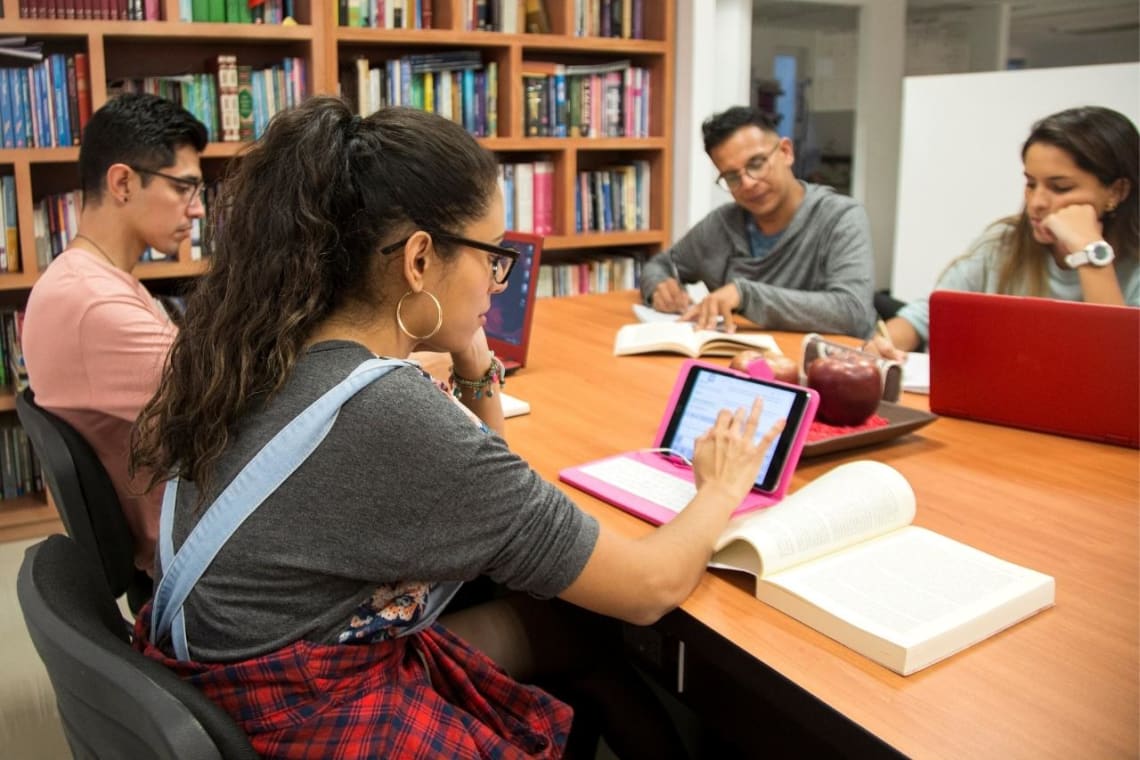 Girl with a tablet and book in a library, learning Spanish on her own