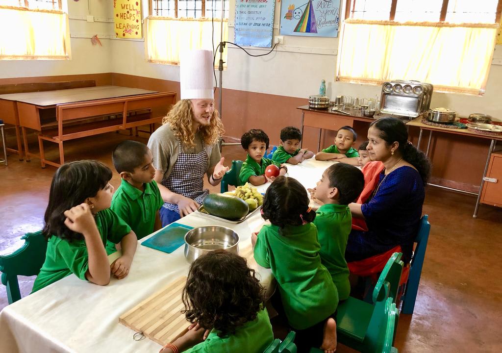 Western guy giving a cooking lesson to kids from a school in India during his gap year volunteering