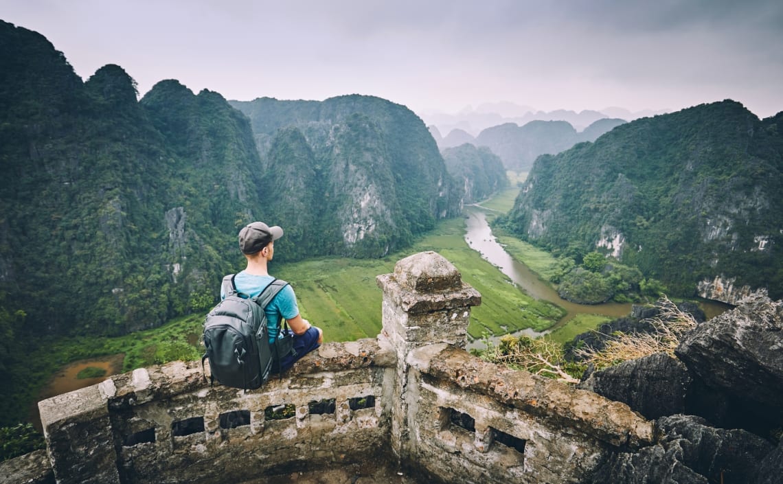 Joven con mochila sentado mirando hacia paisaje natural de China. Viajar ligero es fundamental para hacerlo más cómodamente