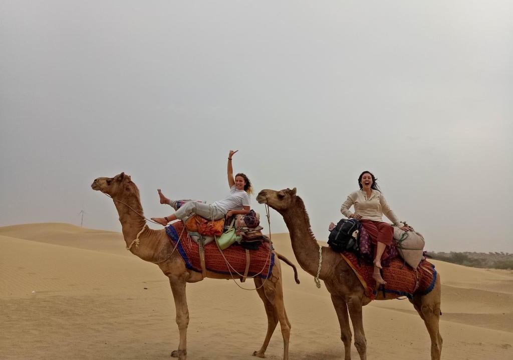 mulheres posam sentadas em camelos num deserto da Íni