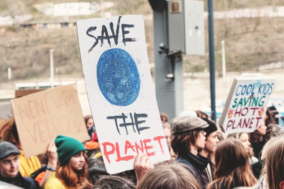 Persona levantando un cartel que dice "Save the planet" en una protesta