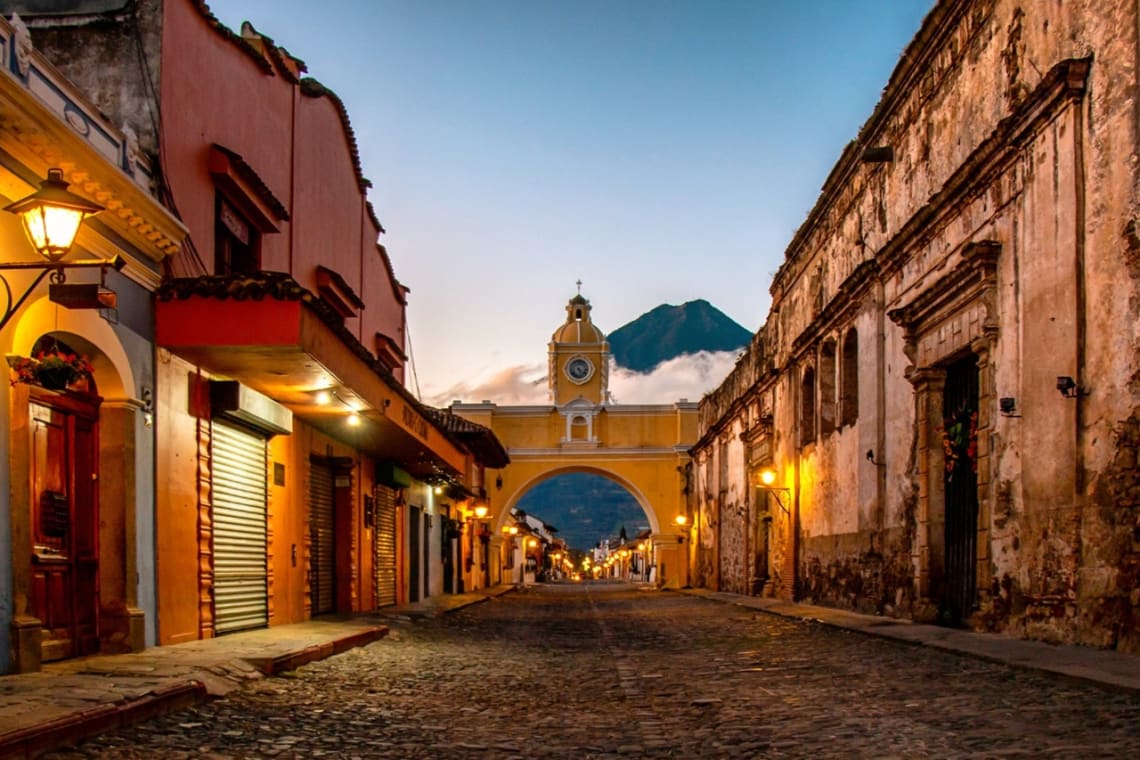 Calle empedrada de Antigua, Guatemala al atardecer con volcán de fondo