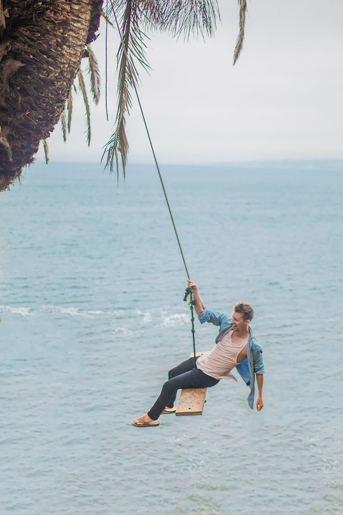 Happy solo traveler swinging over the ocean