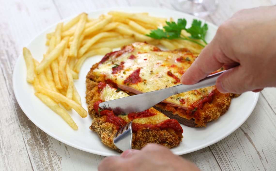 Cortando una milanesa a la napolitana con papas fritas