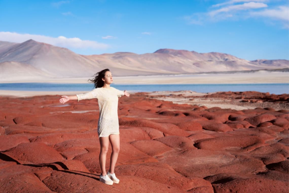 Chica con brazos abiertos disfrutando en las piedras rojas junto a laguna de Aguas Calientes
