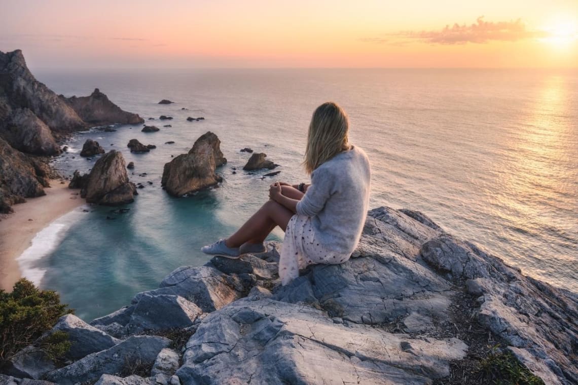 Chica mirando desde lo alto a una playa en Portugal