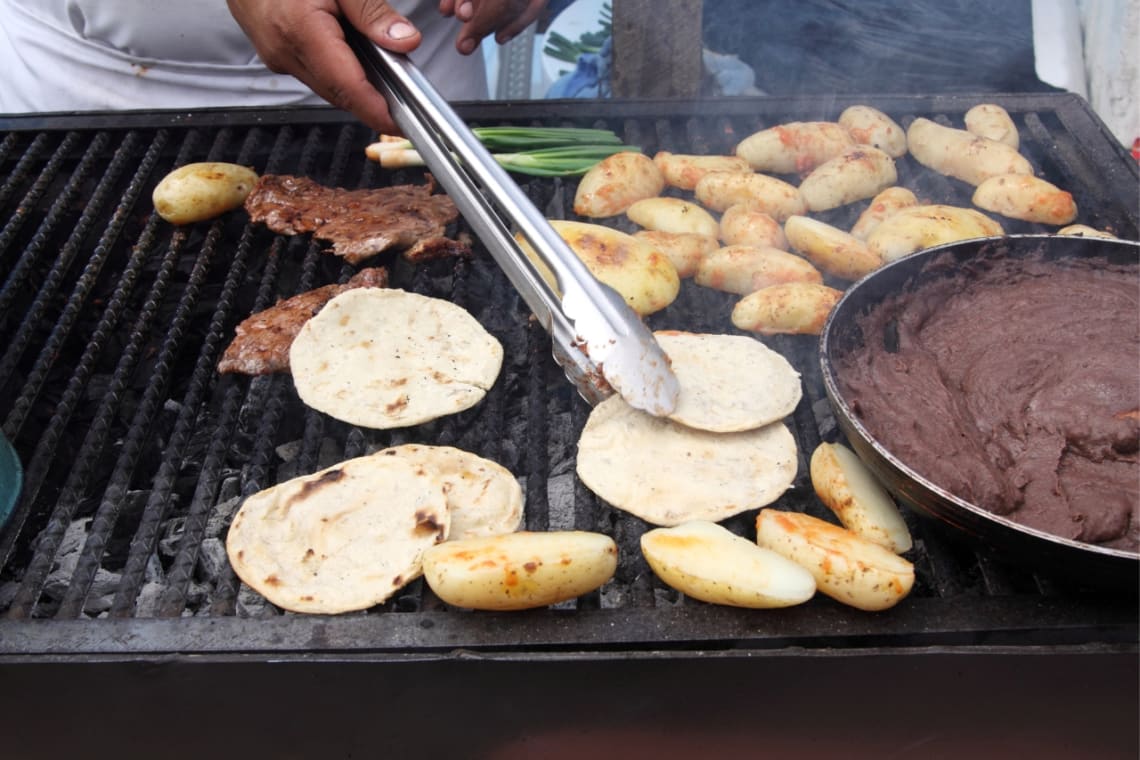Hombre cocinando tortillas y papas en parrilla