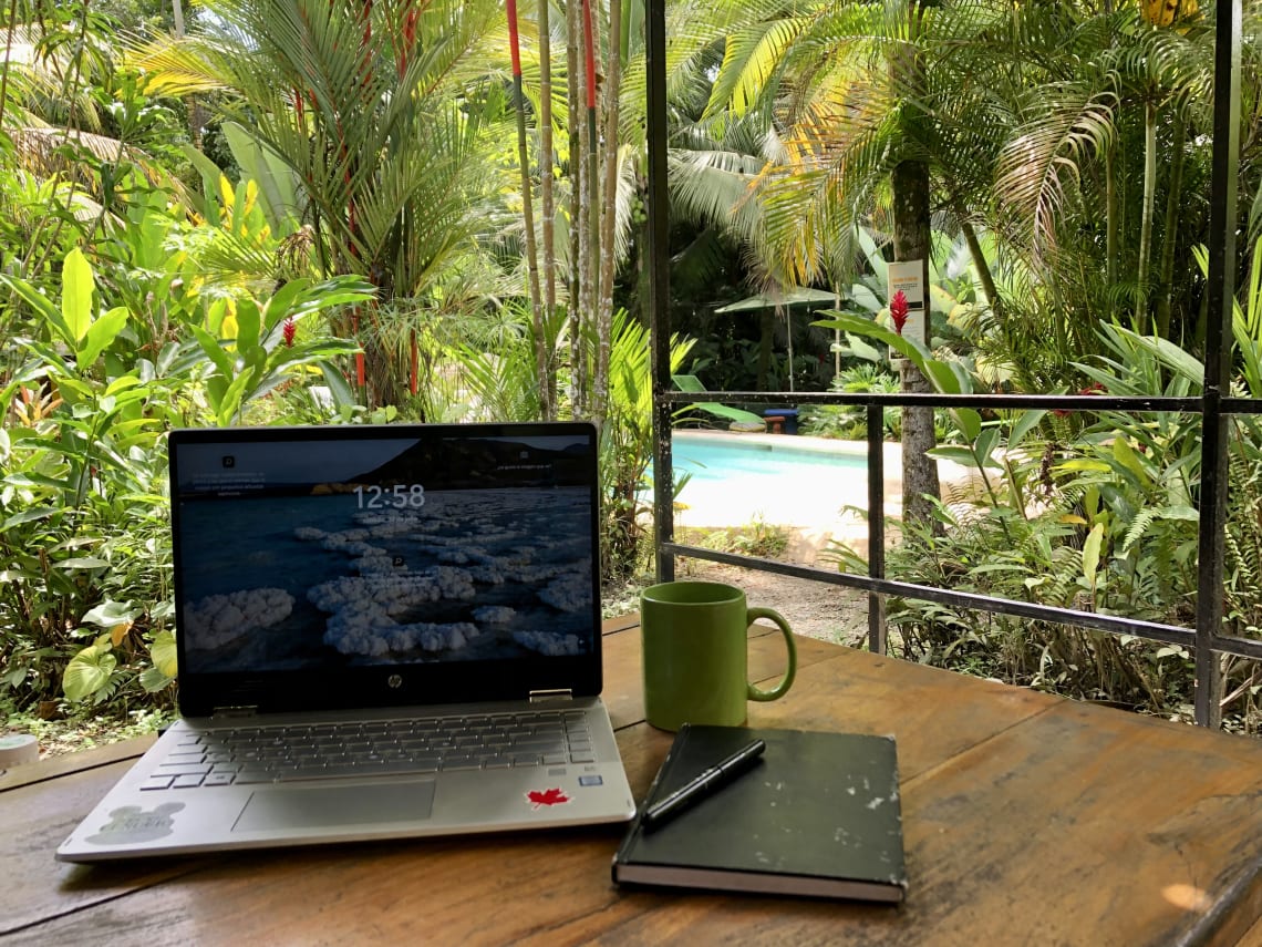Laptop y anotador en mi escritorio rodeado de naturaleza y con vista a una piscina
