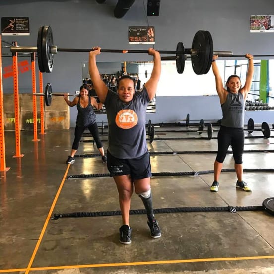 Lindsay Hood, who has a prosthetic leg, stands and raises a weighted barbell above her head.