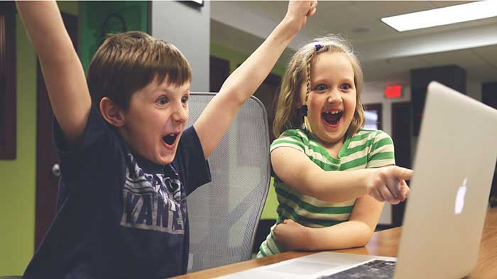 Two kids on the computer with winning excitement.