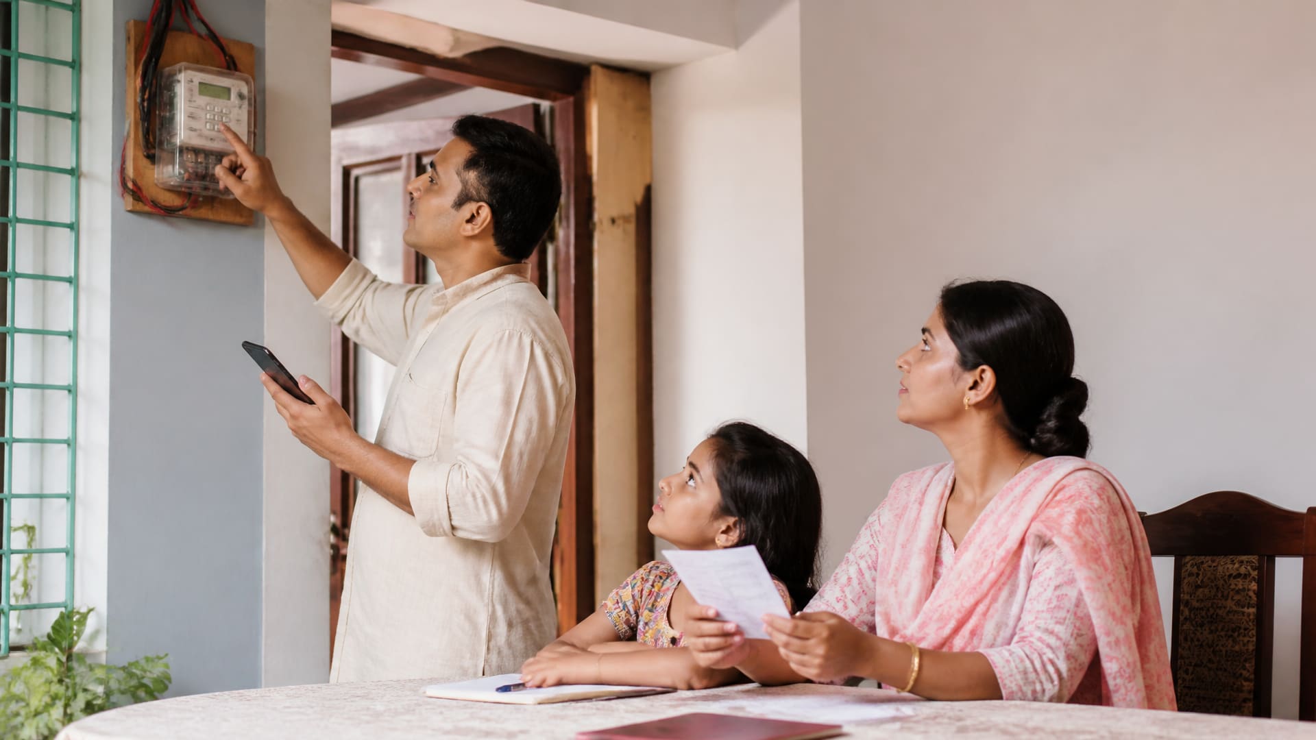 বাংলাদেশের একটি বাসায় একজন ব্যক্তি prepaid electricity meter আর রিচার্জের কাগজ দেখে সমস্যা বুঝছেন।
