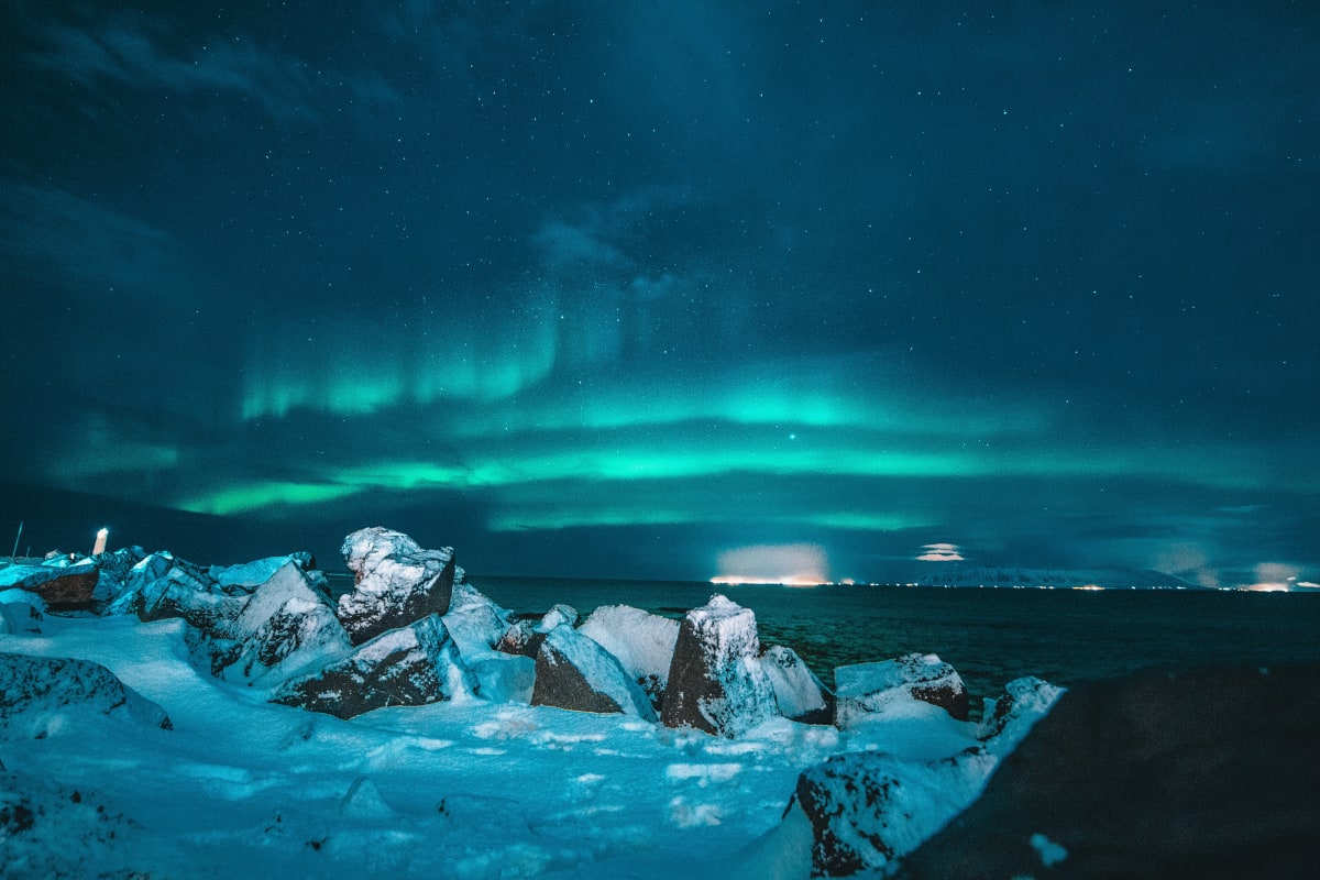 Green aurora borealis over a snowy coastline at night