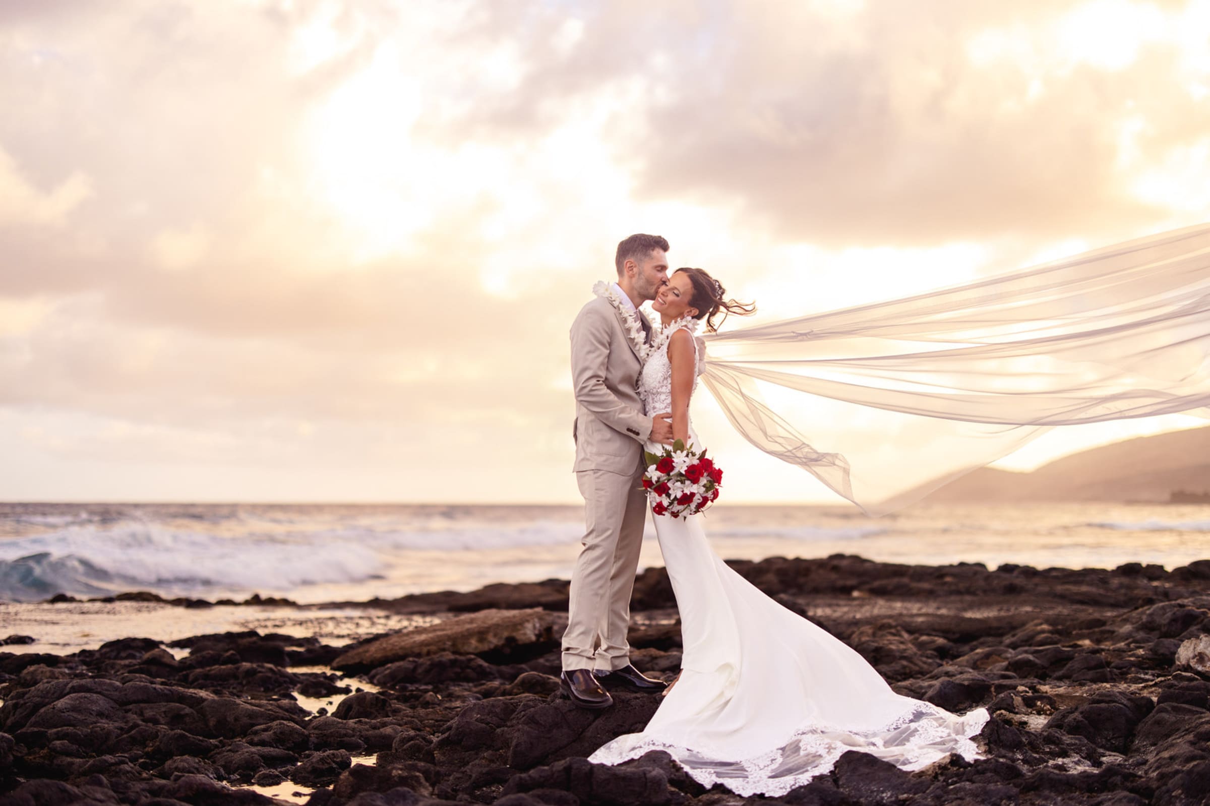 A couple embracing on the lava rocks at sunset, photographed by Carson James Photography
