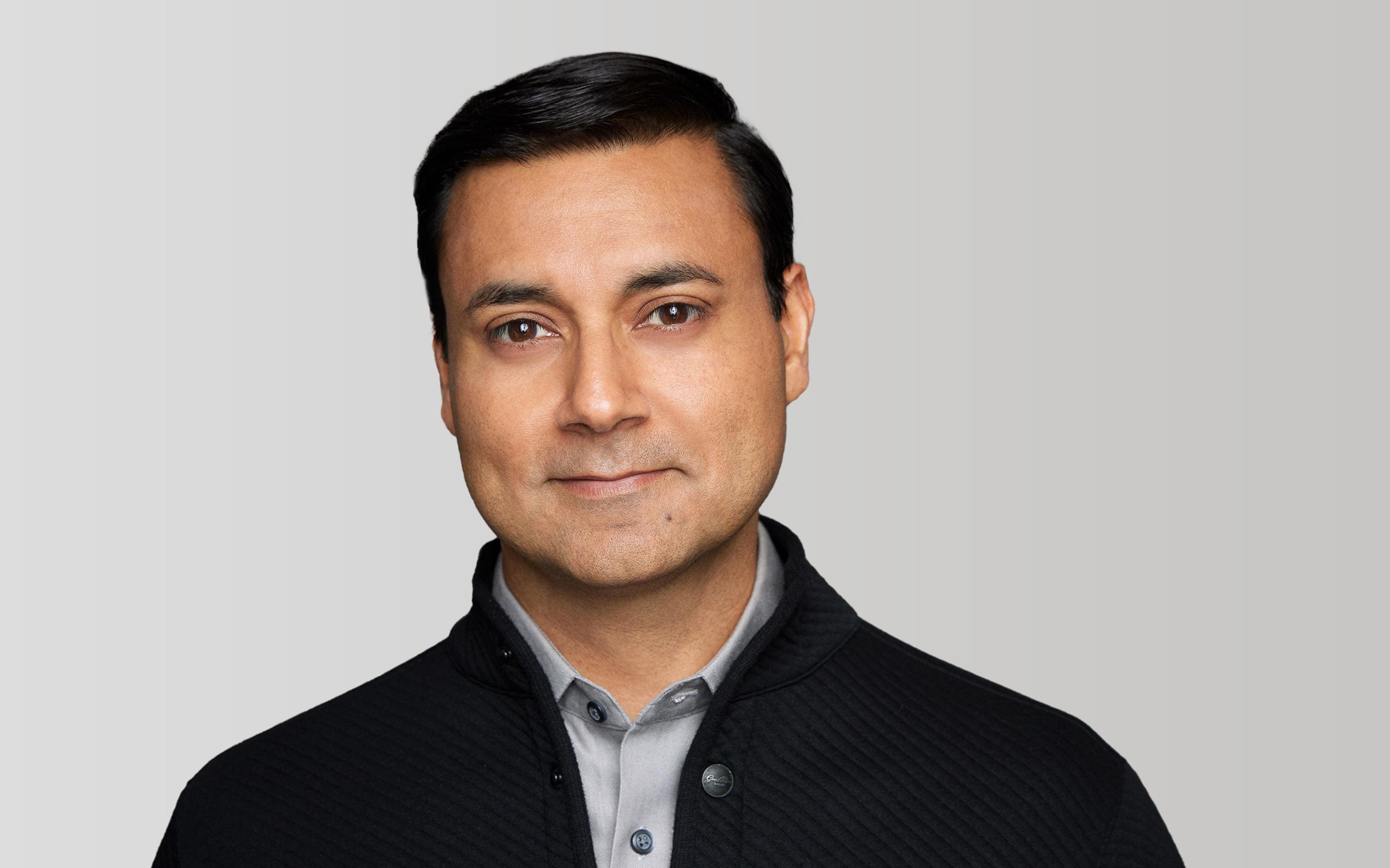 Professional headshot of a man in a black cardigan and blue shirt