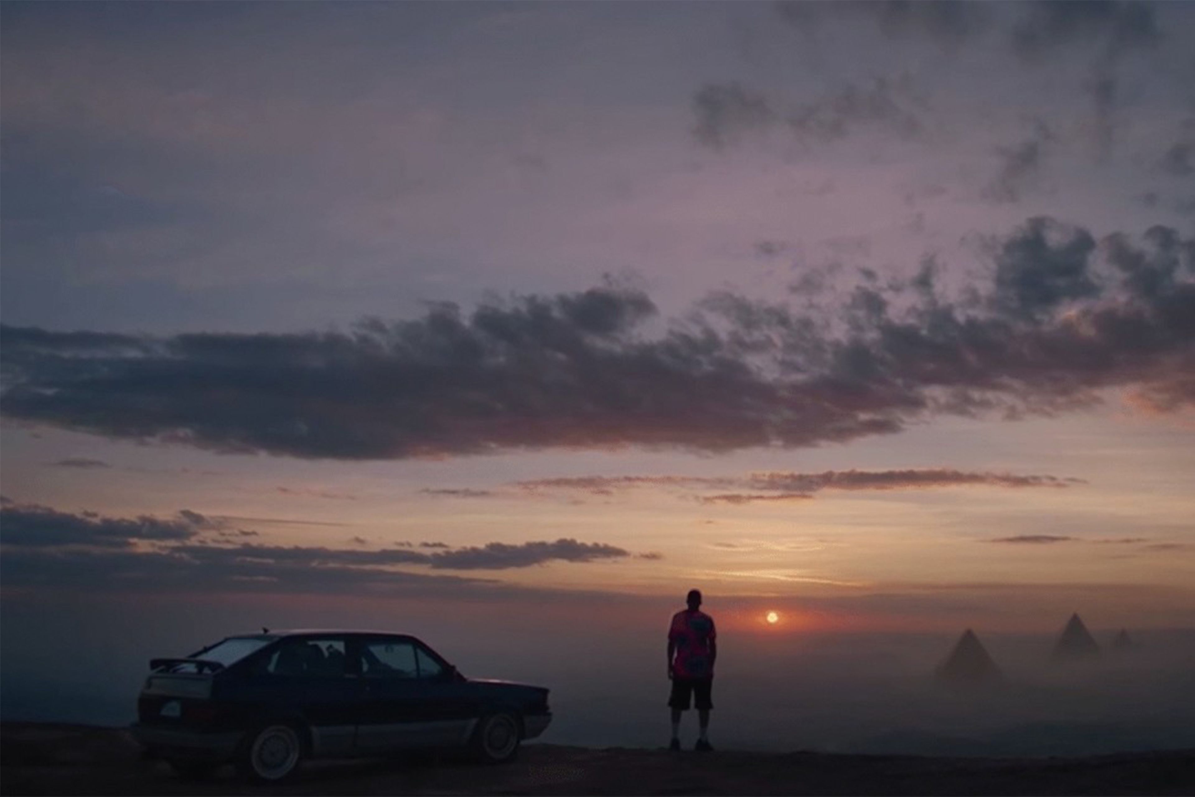 Figure by a car looking out over the sunset